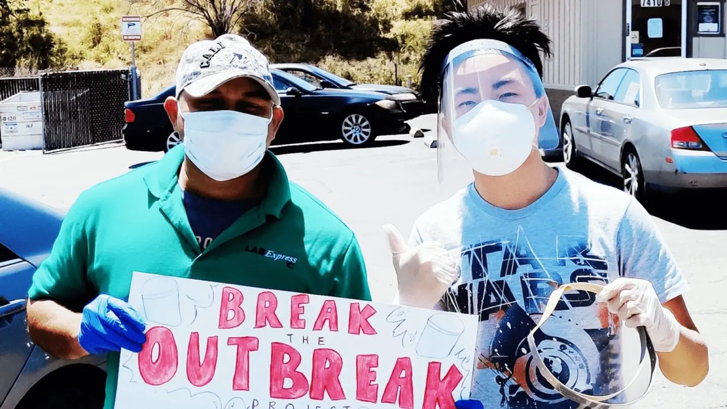 A Break the Outbreak volunteer in a homemade face shield beside a local worker